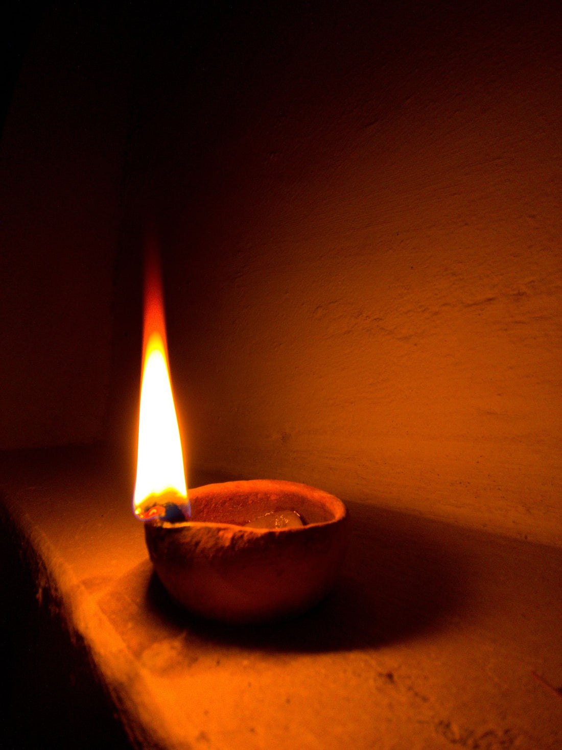 A single clay diya burning in a dark room, the evening lamp of Kartik month