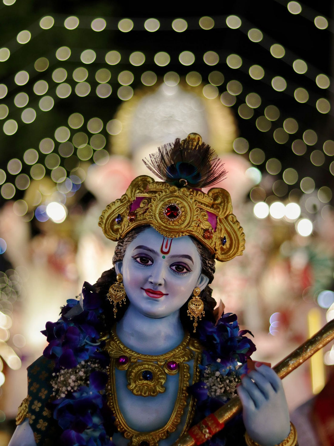 A Krishna murti in a gold crown and peacock feather, lit by festival lights at night